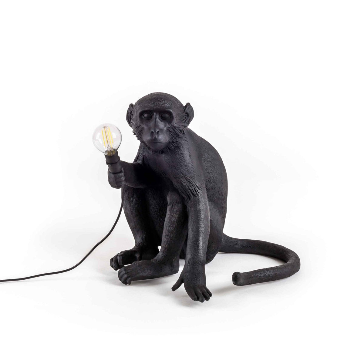 A black monkey table lamp holding a glowing bulb, suitable for a unique home decor style.