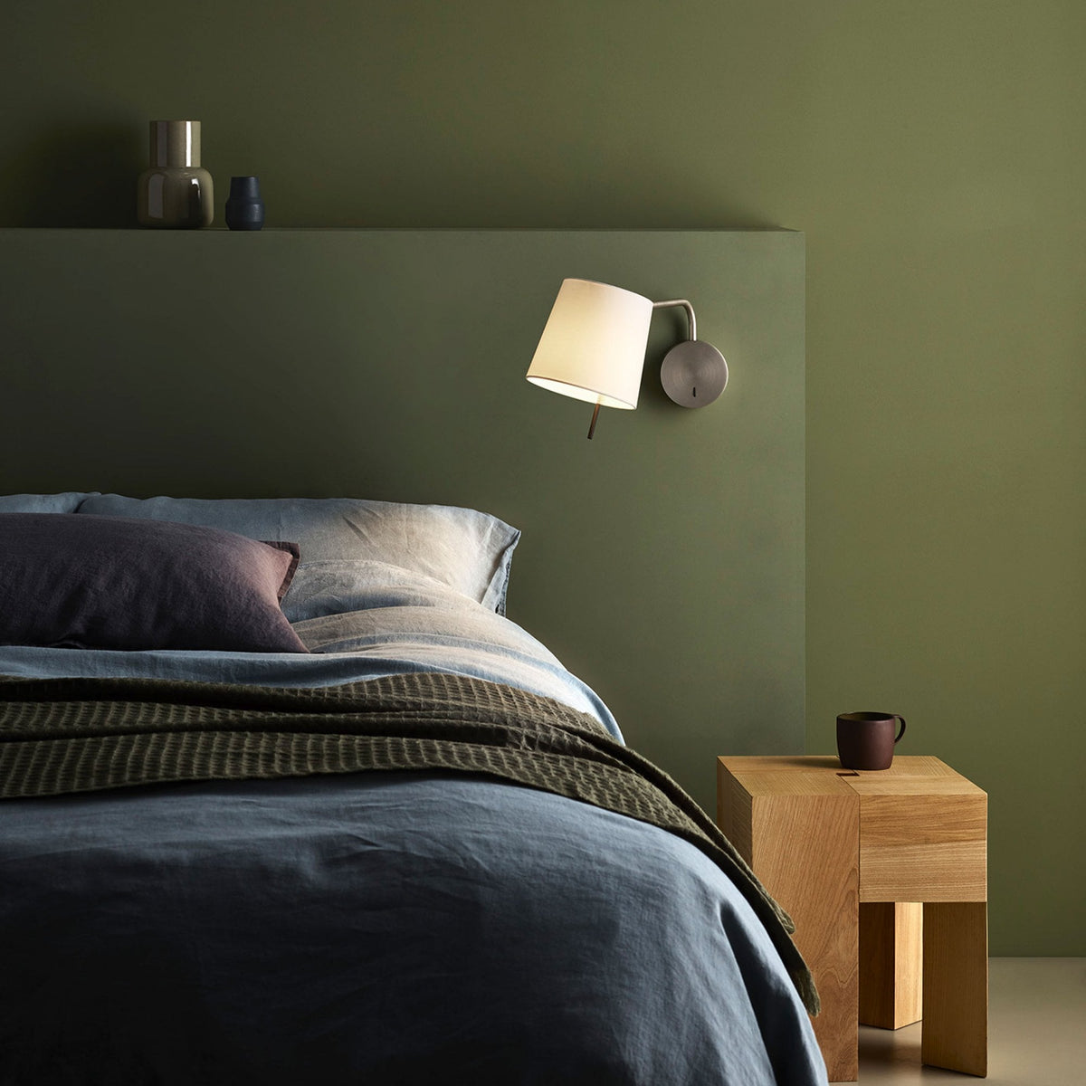 Bedroom with green walls, blue bedding, and a wooden nightstand with a mug