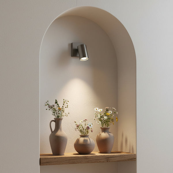 Wall niche with a spotlight illuminating three vases of wildflowers on a wooden shelf