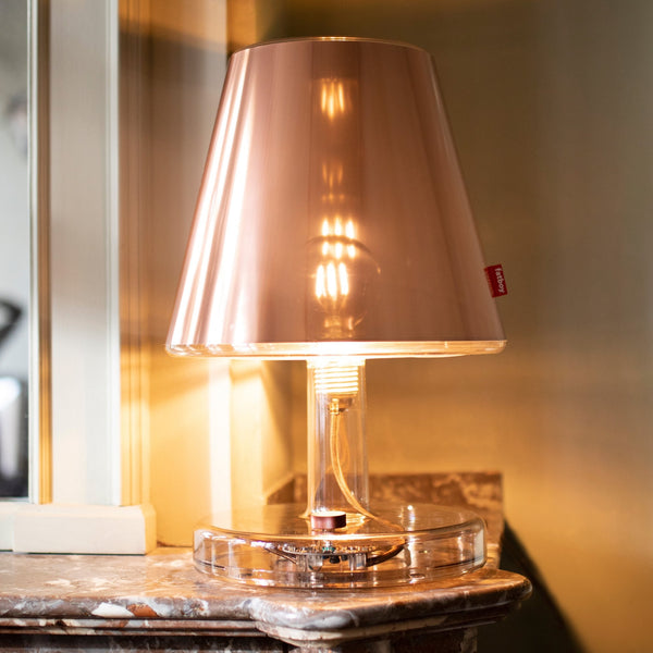 A lit copper-coloured table lamp with a transparent base, on a decorative marble surface.
