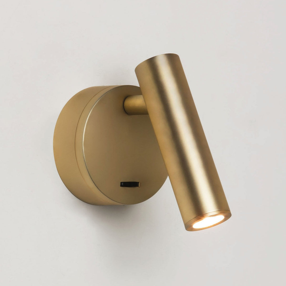 Brass wall-mounted reading light with a cylindrical head and a circular base