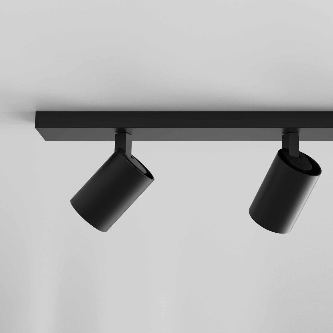 Two black cylindrical track lights on a black track against a white ceiling