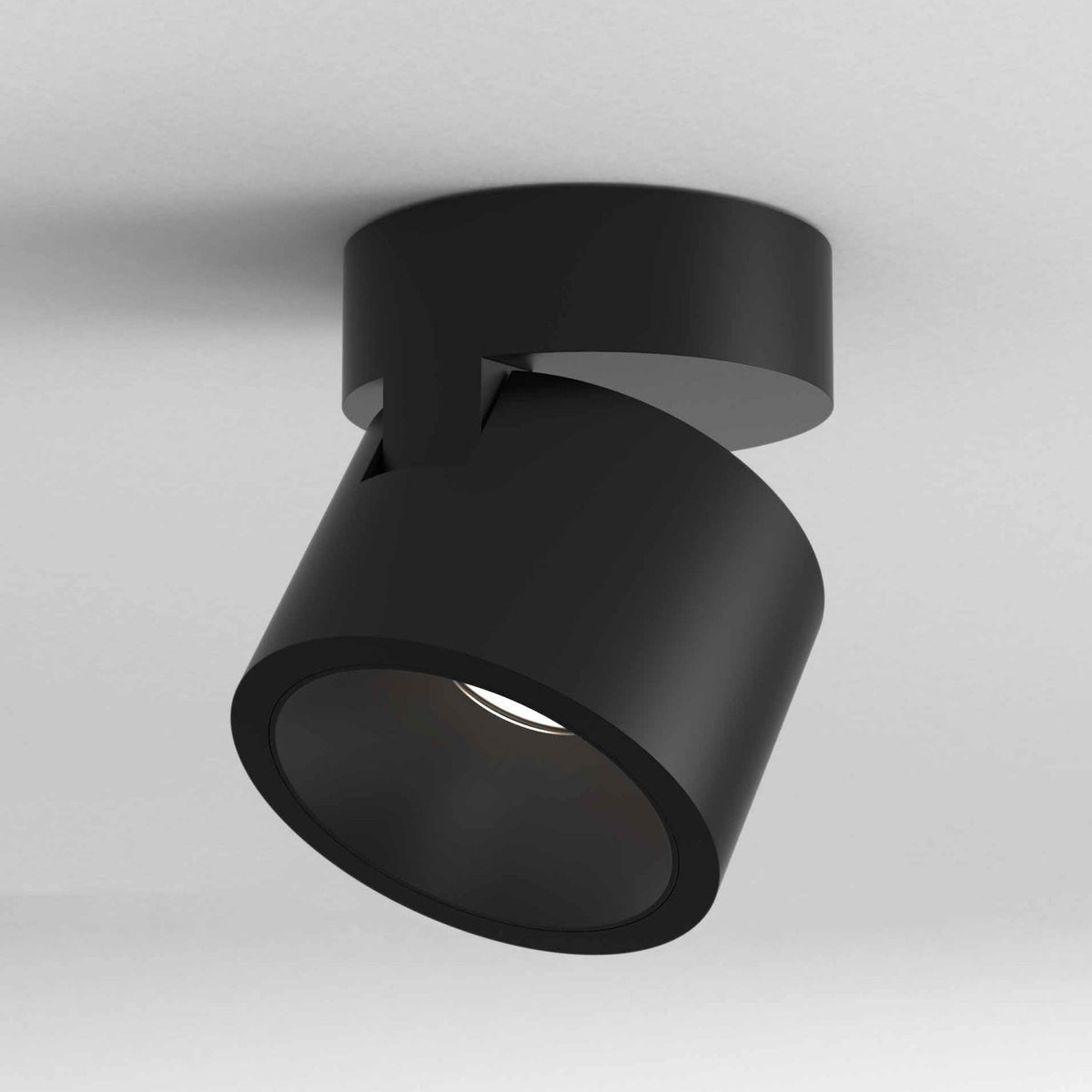 Black cylindrical ceiling spotlight with an adjustable head, angled downwards and emitting a soft glow