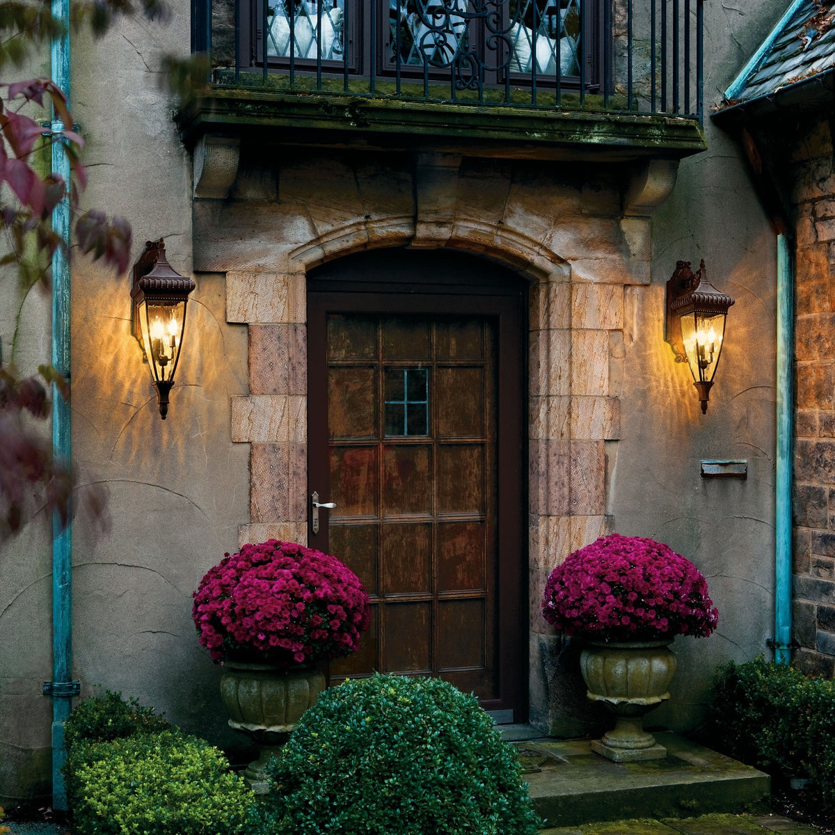Two illuminated ornate bronze outdoor wall lights flank a traditional doorway.