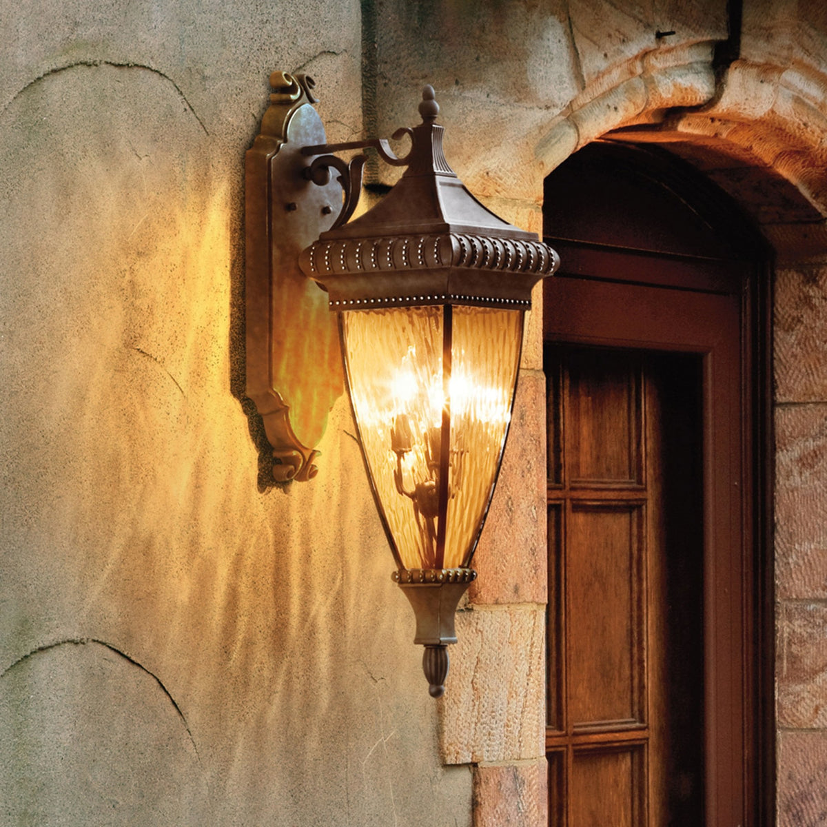 An ornate bronze outdoor wall light with fluted glass illuminating a wall.