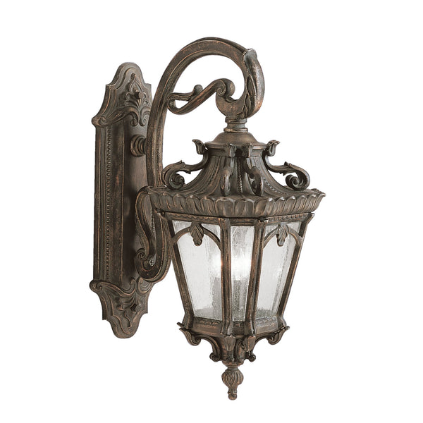 A full view of a bronze outdoor wall light with an ornate bracket and seeded glass panels.