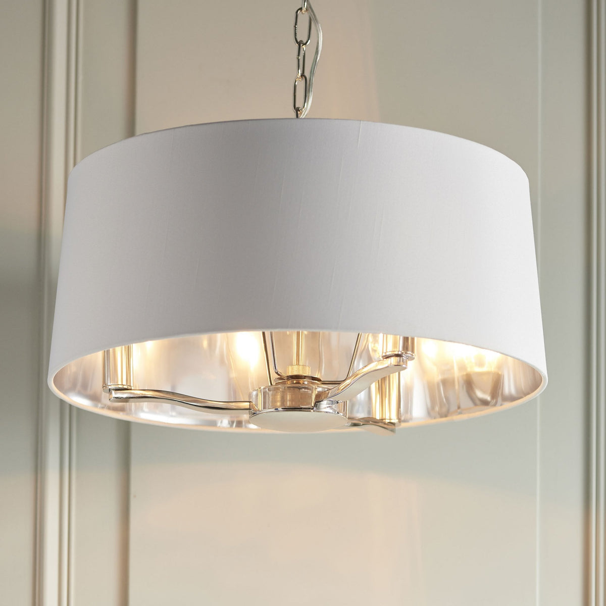 White drum pendant light with polished nickel accents and exposed bulbs, hanging in a room.