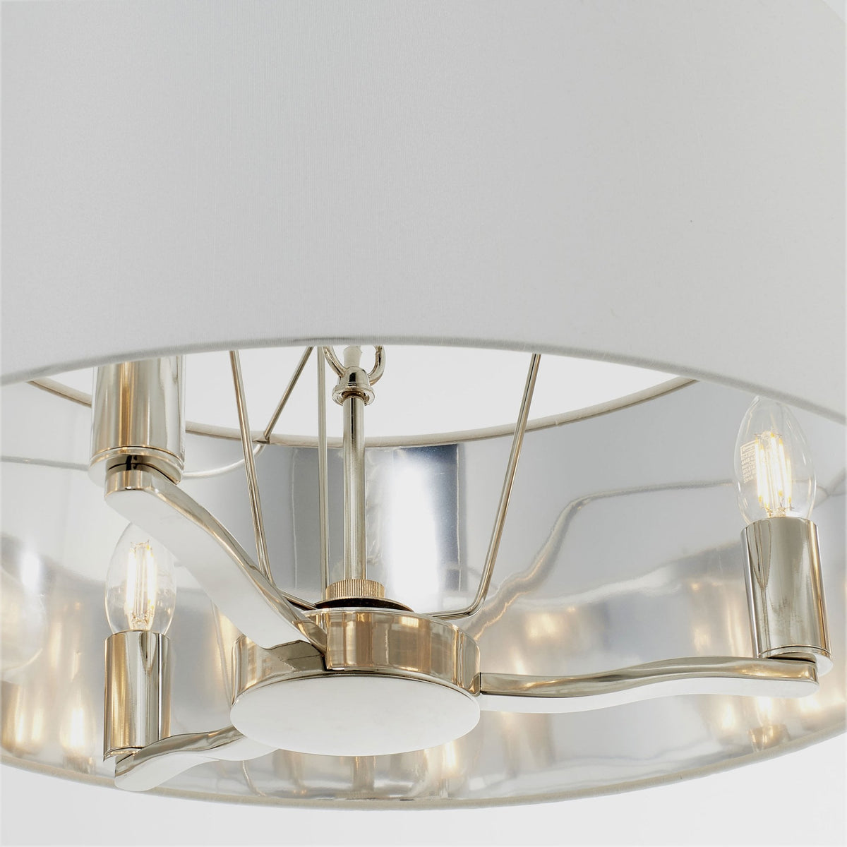 Close-up of the polished nickel frame and exposed bulbs inside a white drum pendant light.