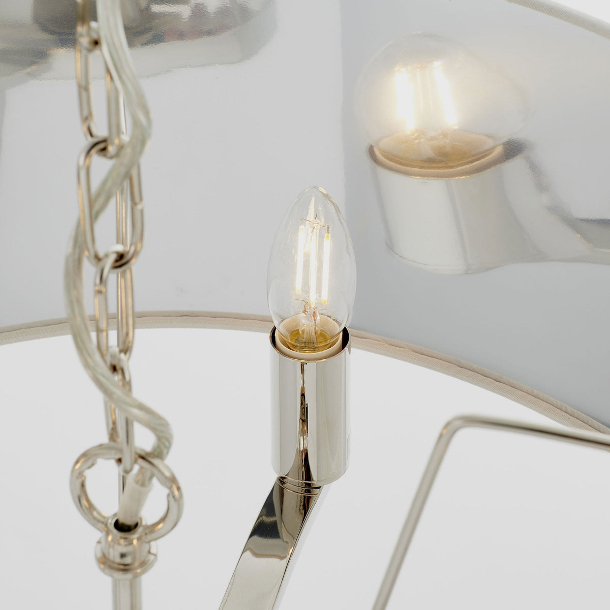 Close-up of an illuminated bulb and polished nickel chain of a pendant light.