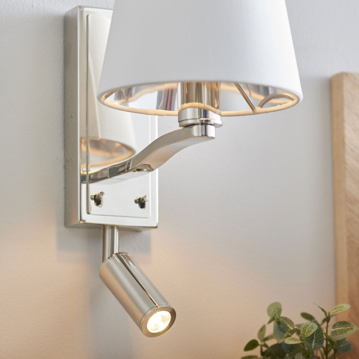 Close-up of a polished nickel wall light with a white fabric shade and an adjustable reading light.