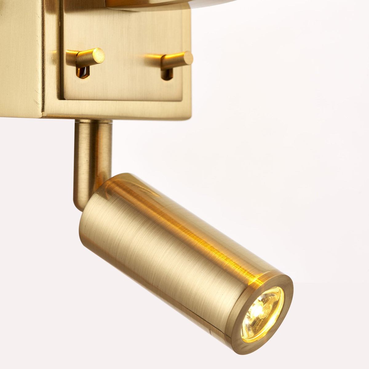 Close-up of the adjustable brass spotlight on a wall light, emitting a warm glow.