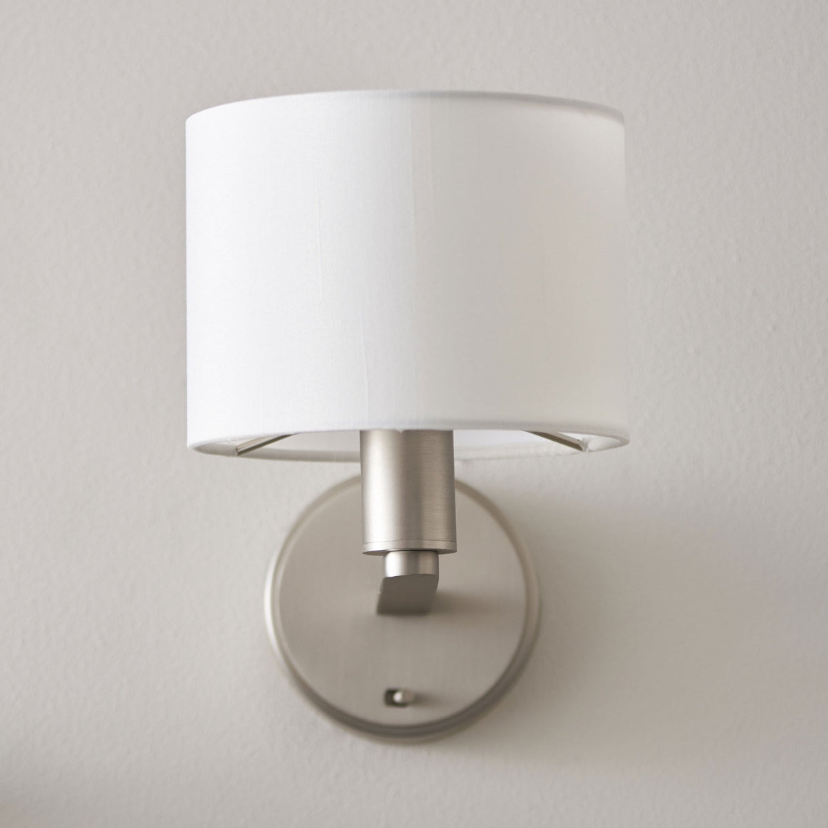 Wall-mounted lamp with a white cylindrical shade and brushed nickel base, positioned vertically on a light wall.