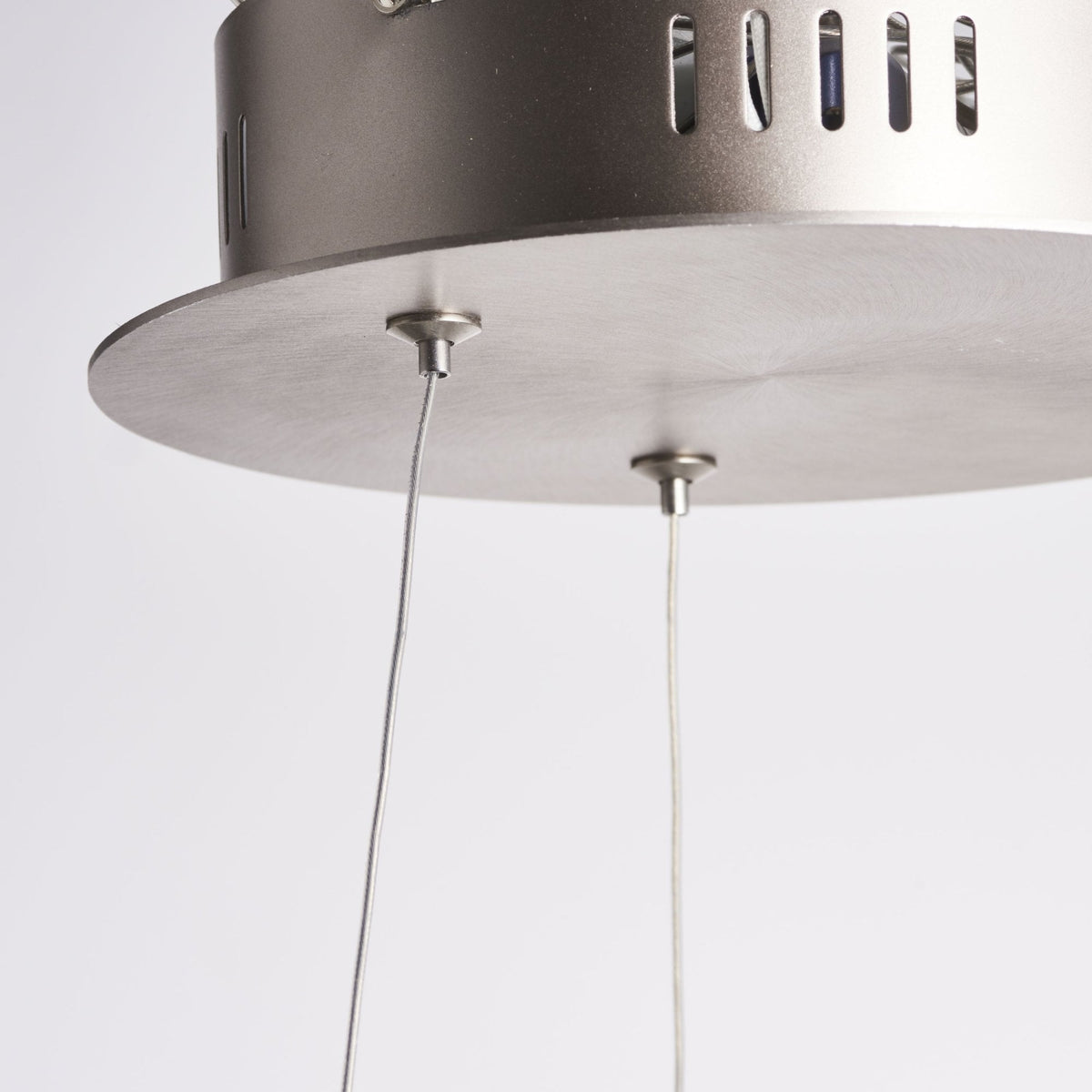 Close-up of the ceiling mount and suspension wires of a circular LED pendant light.