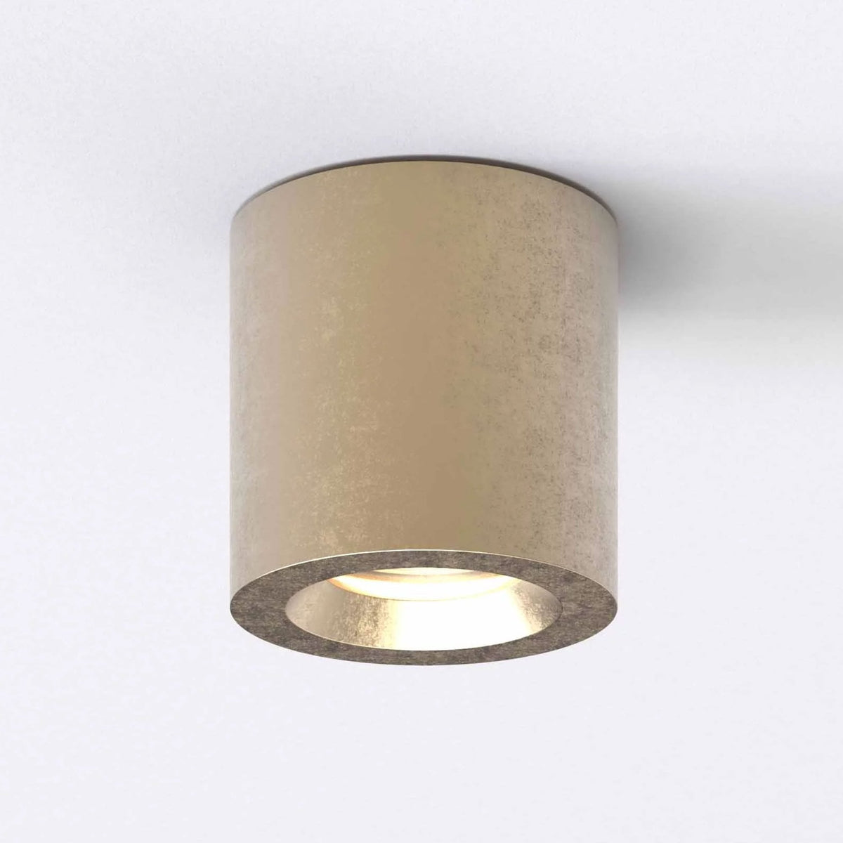 Cylindrical ceiling light fixture in a distressed gold finish, emitting a warm glow downwards