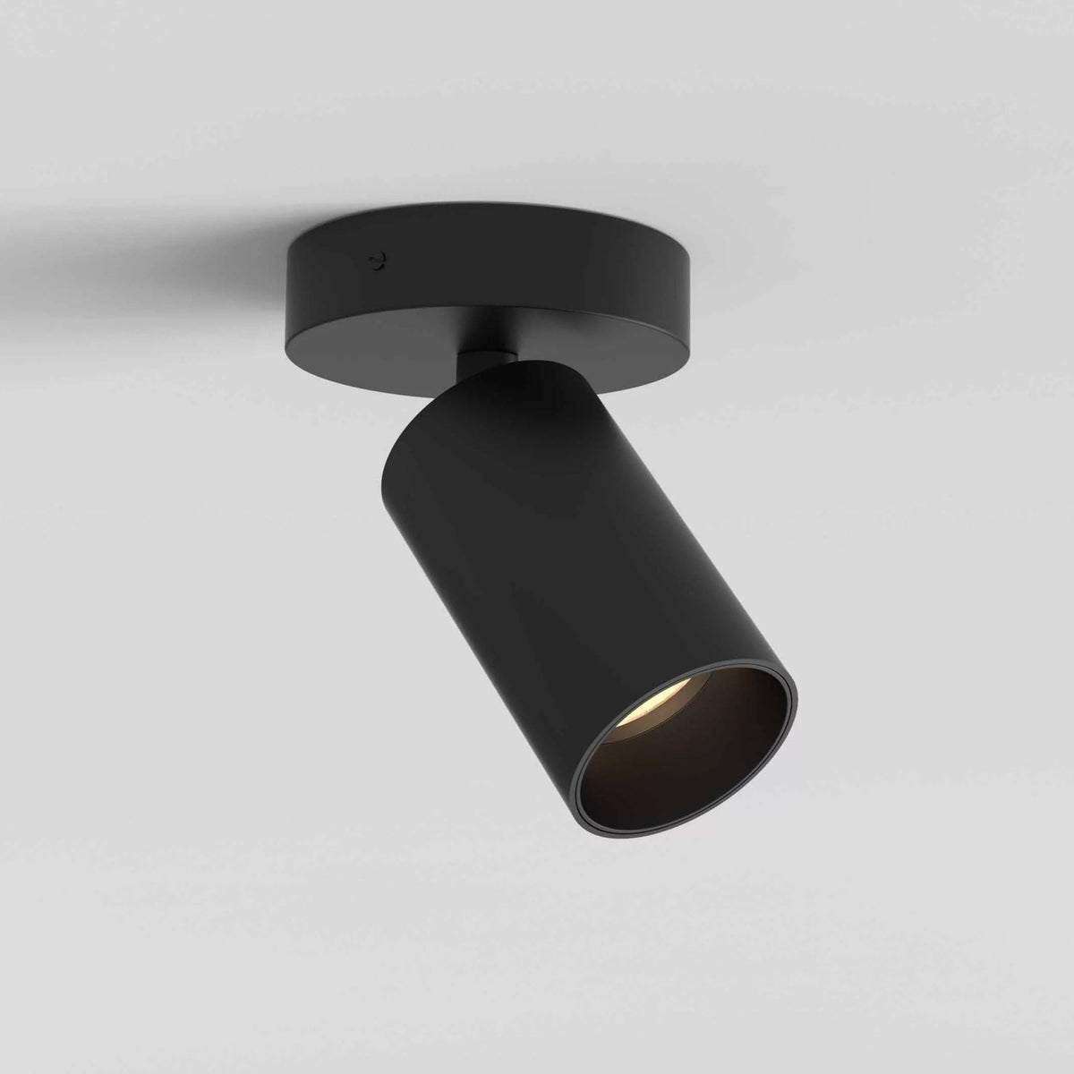 Black cylindrical ceiling spotlight with a warm light, mounted on a round base against a white ceiling