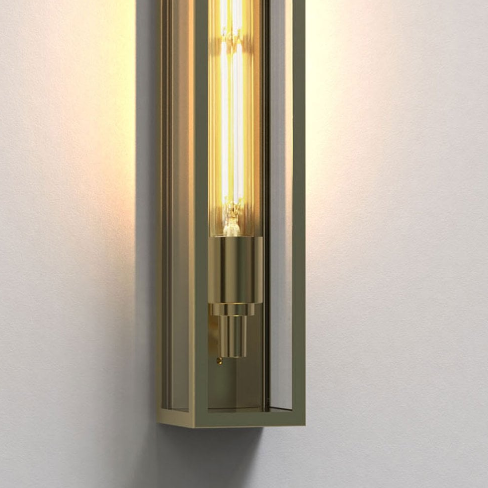 A close-up of a gold-colored wall sconce with a long, exposed filament bulb