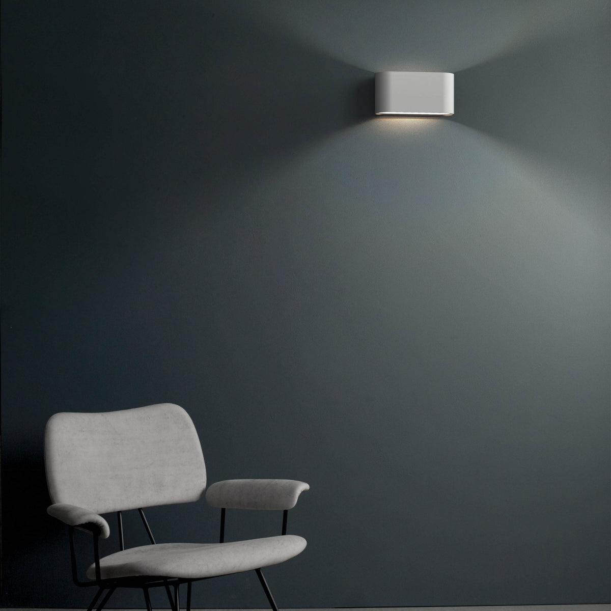 White rectangular wall light illuminating a dark grey wall above a light grey upholstered chair