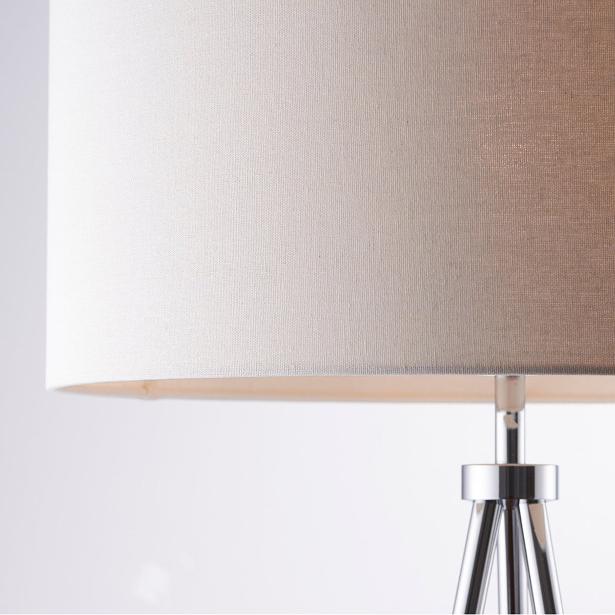 Close-up of a beige drum lampshade and the top of a silver tripod lamp base.