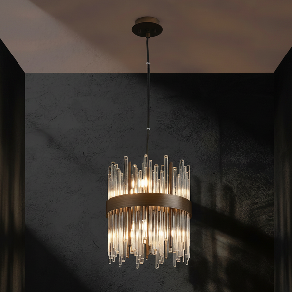 Cylindrical chandelier with clear glass rods and a bronze band, illuminated against a dark textured wall