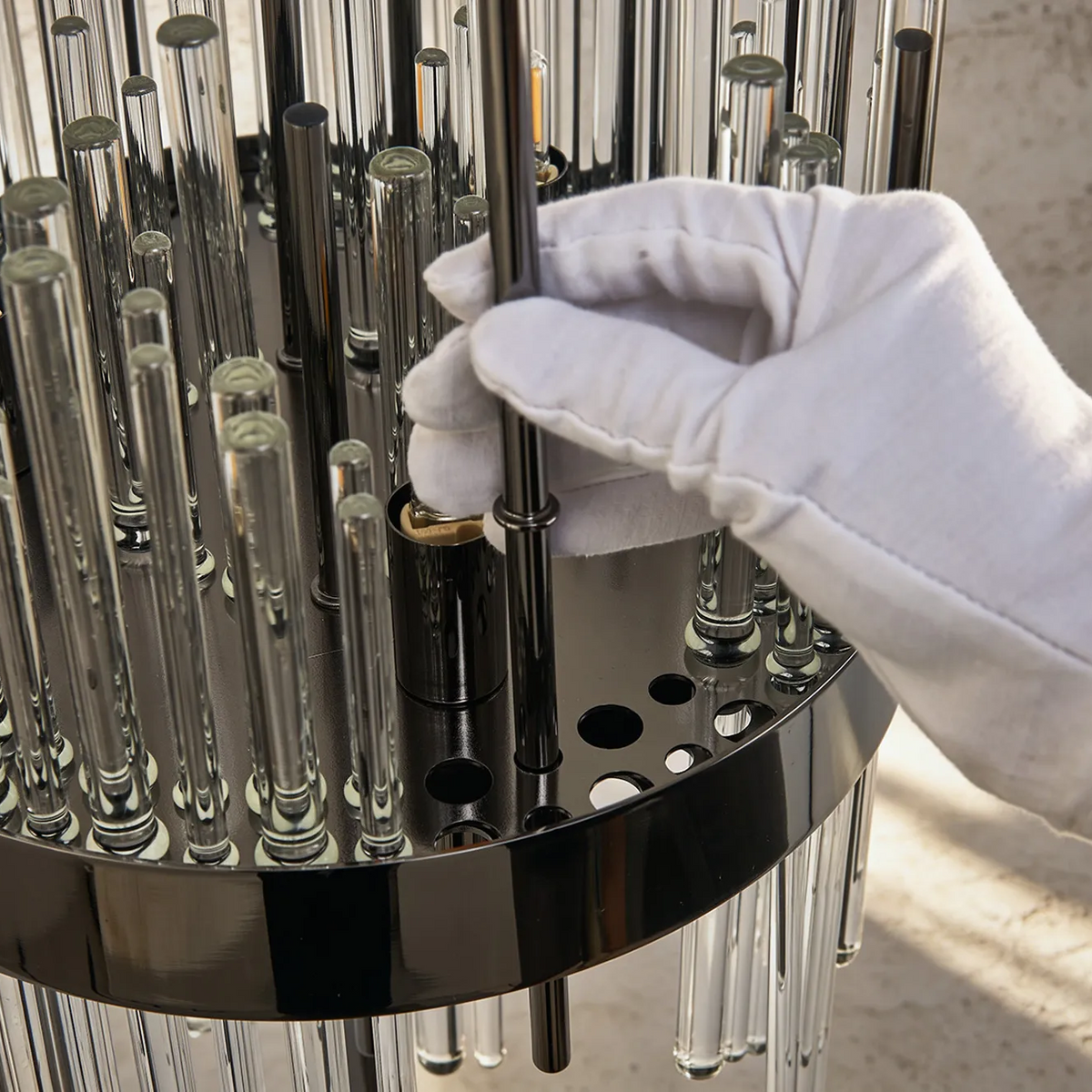 Gloved hand assembling a chandelier with glass rods and a black metal base