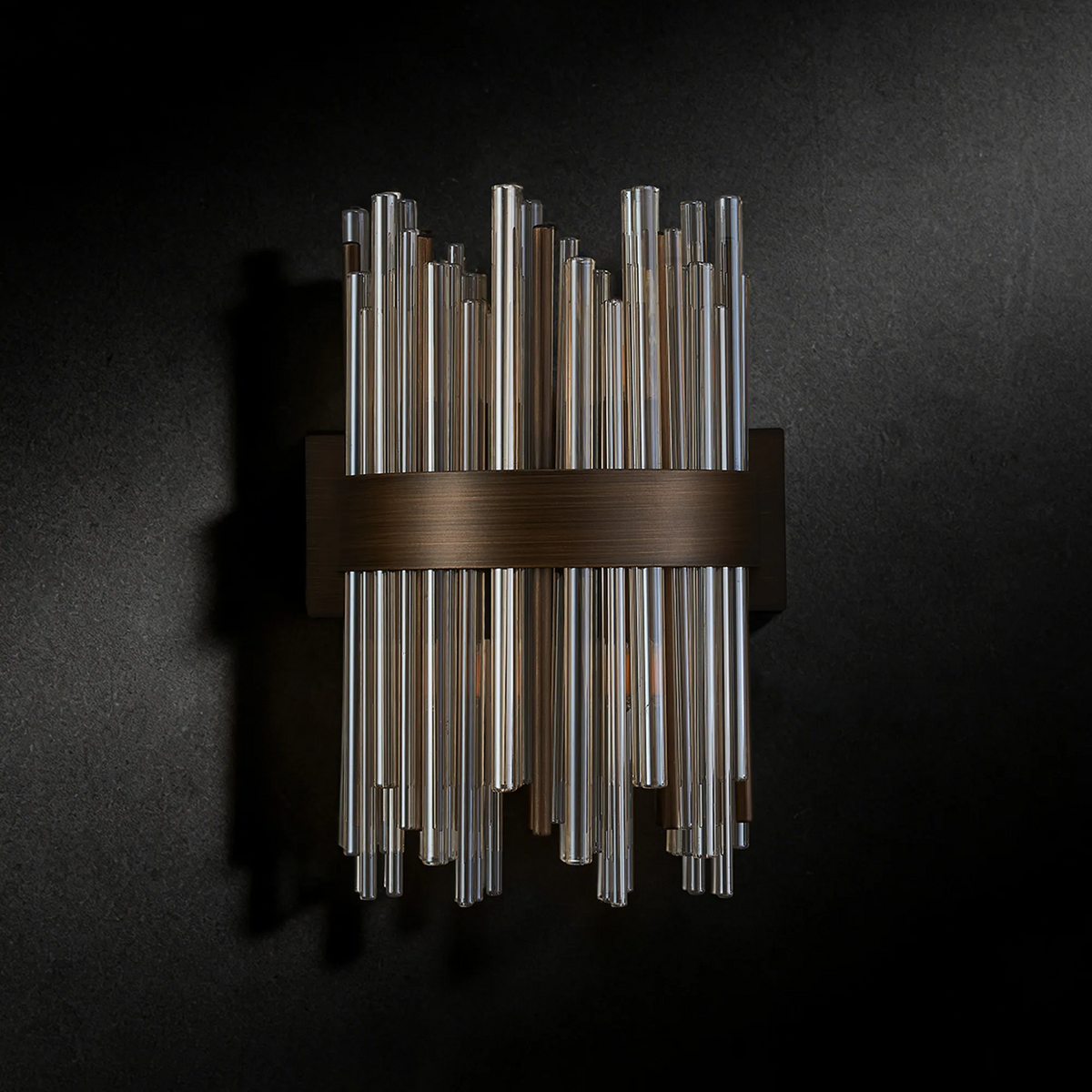 Wall sconce with clear and amber glass rods on a dark bronze backplate