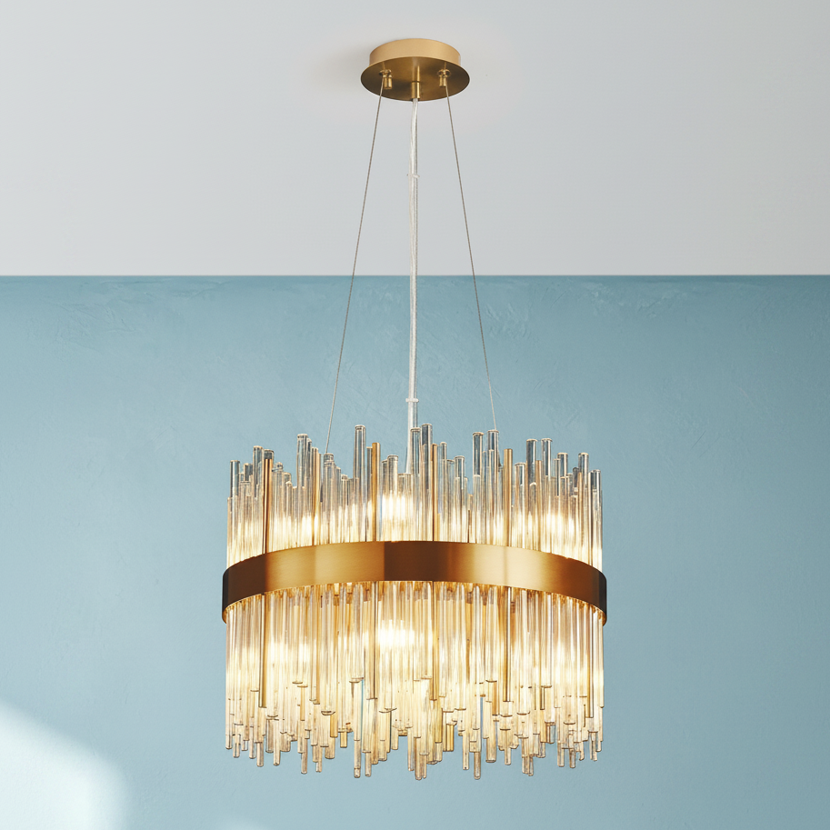 Round gold chandelier with multiple glass rods hanging down, illuminated against a blue wall
