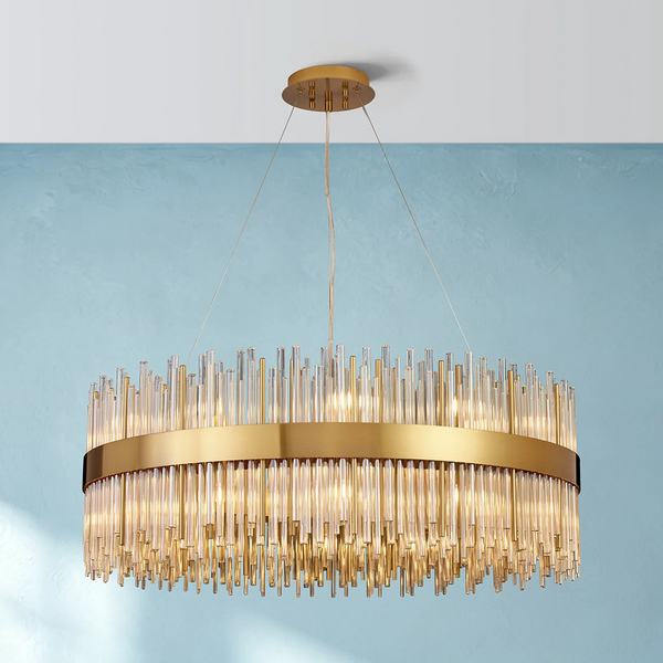 Round gold chandelier with clear glass rods hanging at varying lengths, against a blue wall