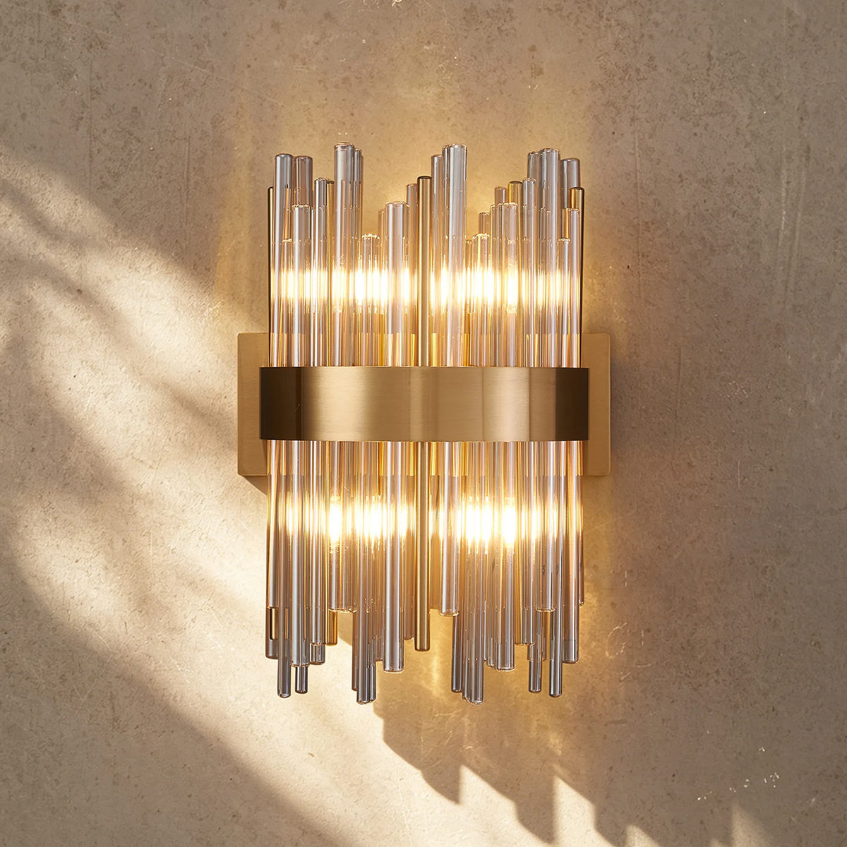 Brass and glass tube wall sconce with warm light on a textured wall