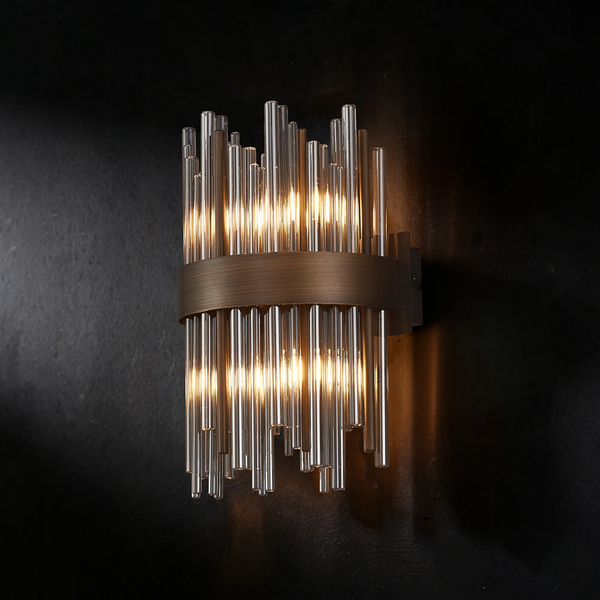 Wall sconce with clear glass rods and a bronze band, illuminated against a dark background
