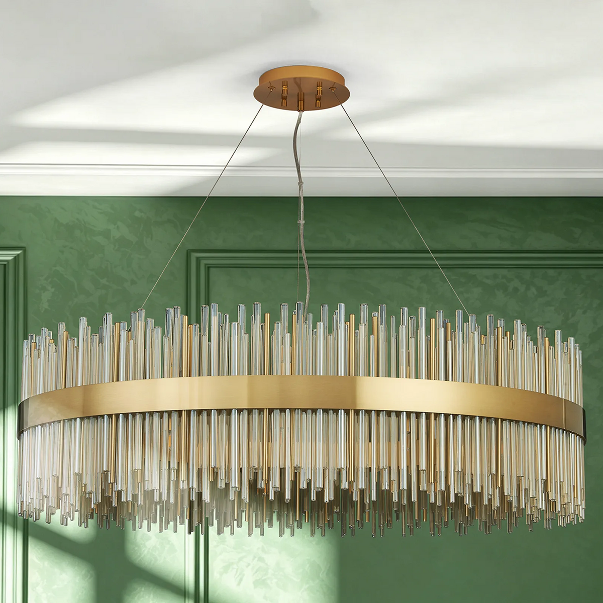 Round gold chandelier with clear and gold glass rods hanging from a white ceiling against a green wall