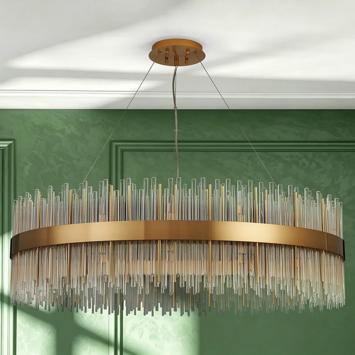 Round chandelier with clear and gold glass rods, brass band, against a green wall