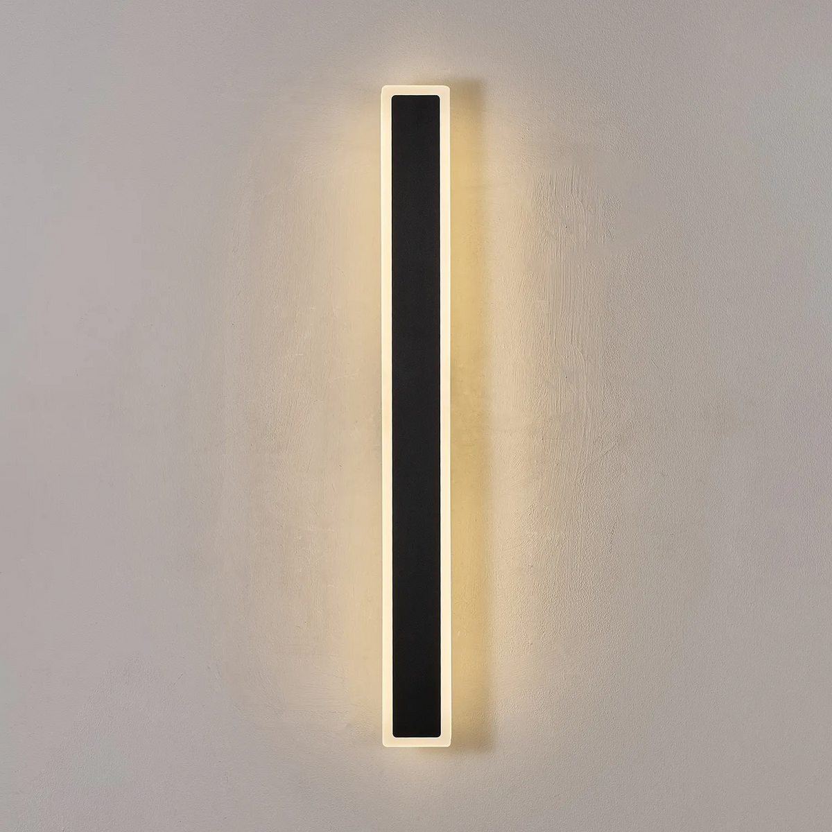 Vertical black and white wall light illuminated on a grey wall