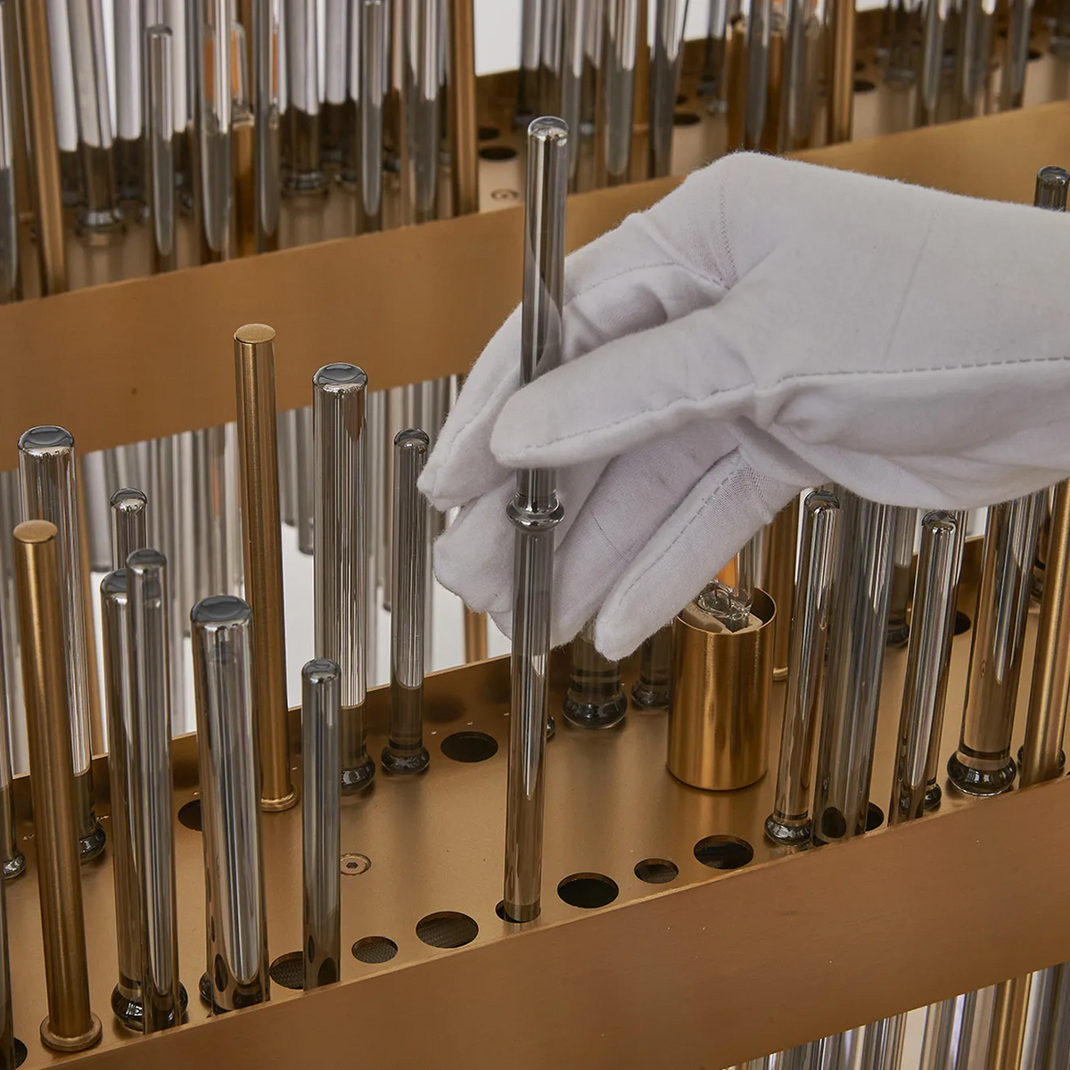 Gloved hand placing a glass rod into a brass holder with many other glass and metal rods