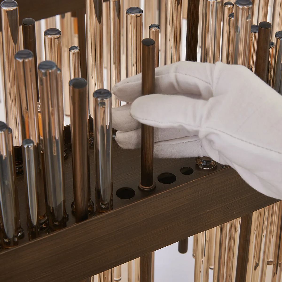 Gloved hand inserting a bronze rod into a chandelier frame with glass rods