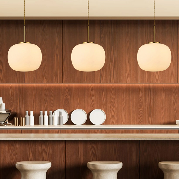 Three Lumiere Milton Medium Oval Ball Pendants in Aged Brass & Frosted White Shade over a wooden bar