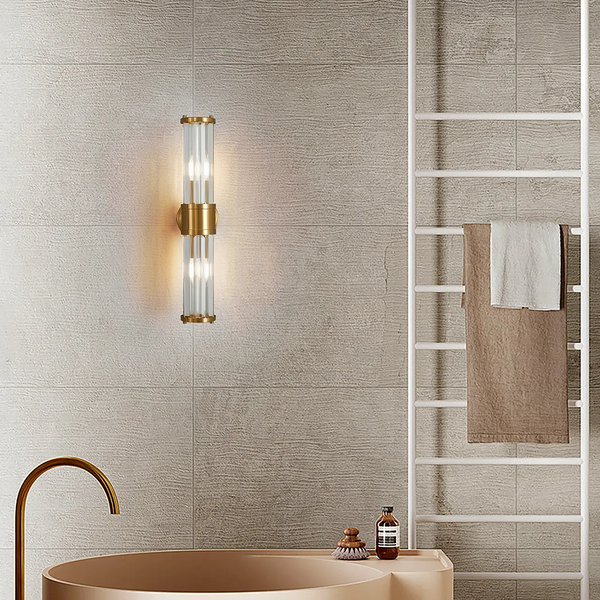 A gold and glass wall sconce illuminates a bathroom with a gold faucet and a towel rack