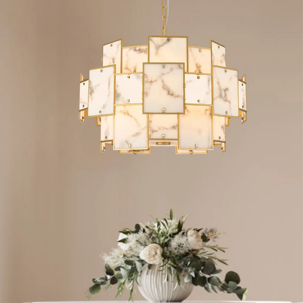 Gold chandelier with square marble panels hanging above a white floral arrangement in a ribbed vase