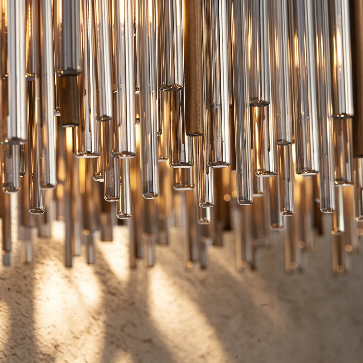 Close-up of a chandelier with numerous glass rods hanging down, illuminated by warm light