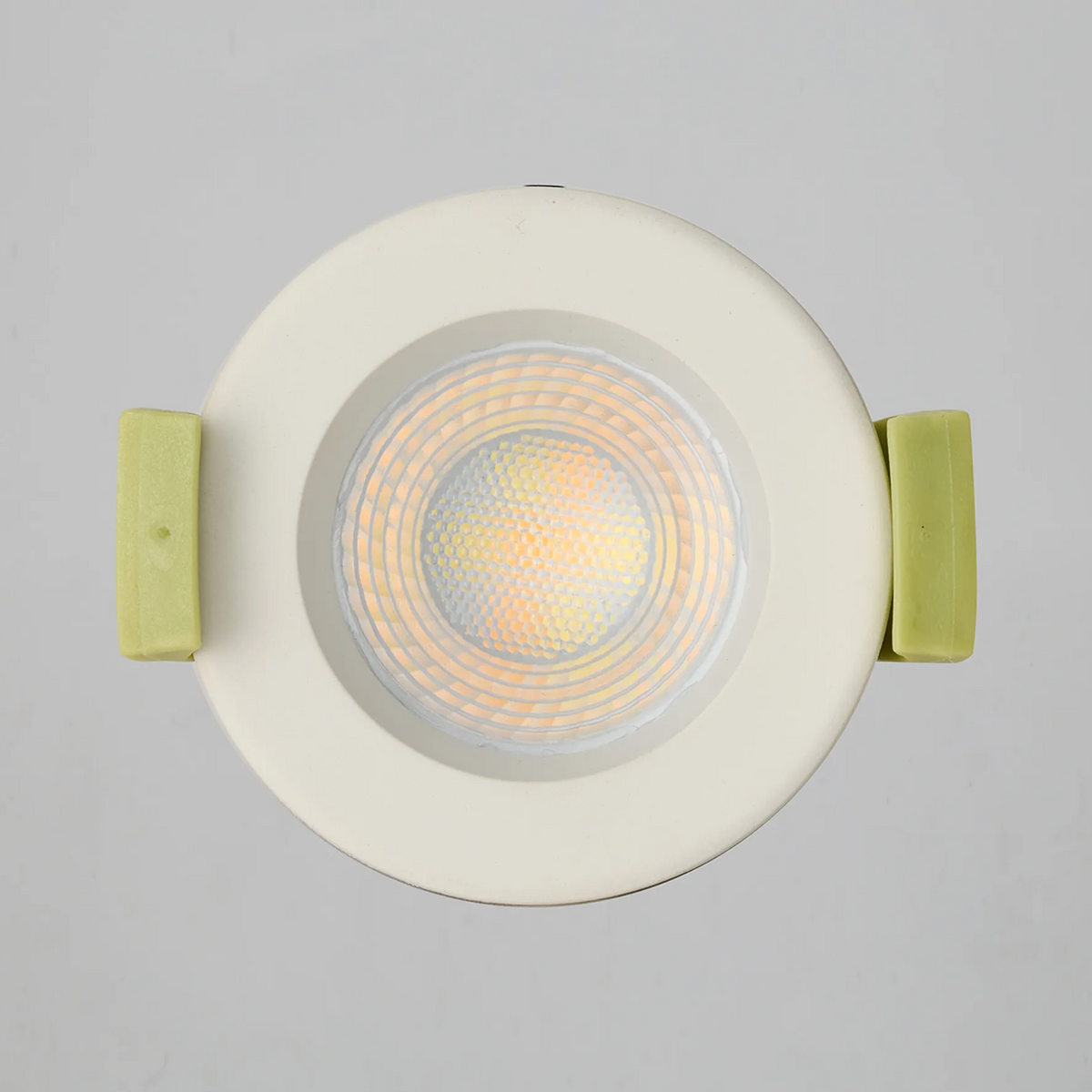 Top down view of a recessed light with a white trim and lime green clips, light is off