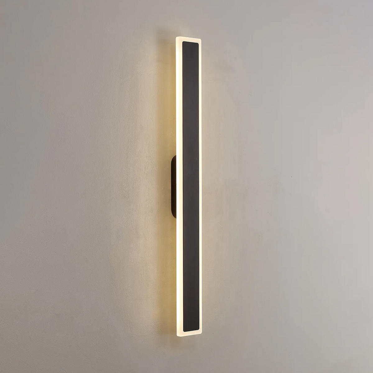 Angled view of an illuminated vertical black and white wall light on a grey wall