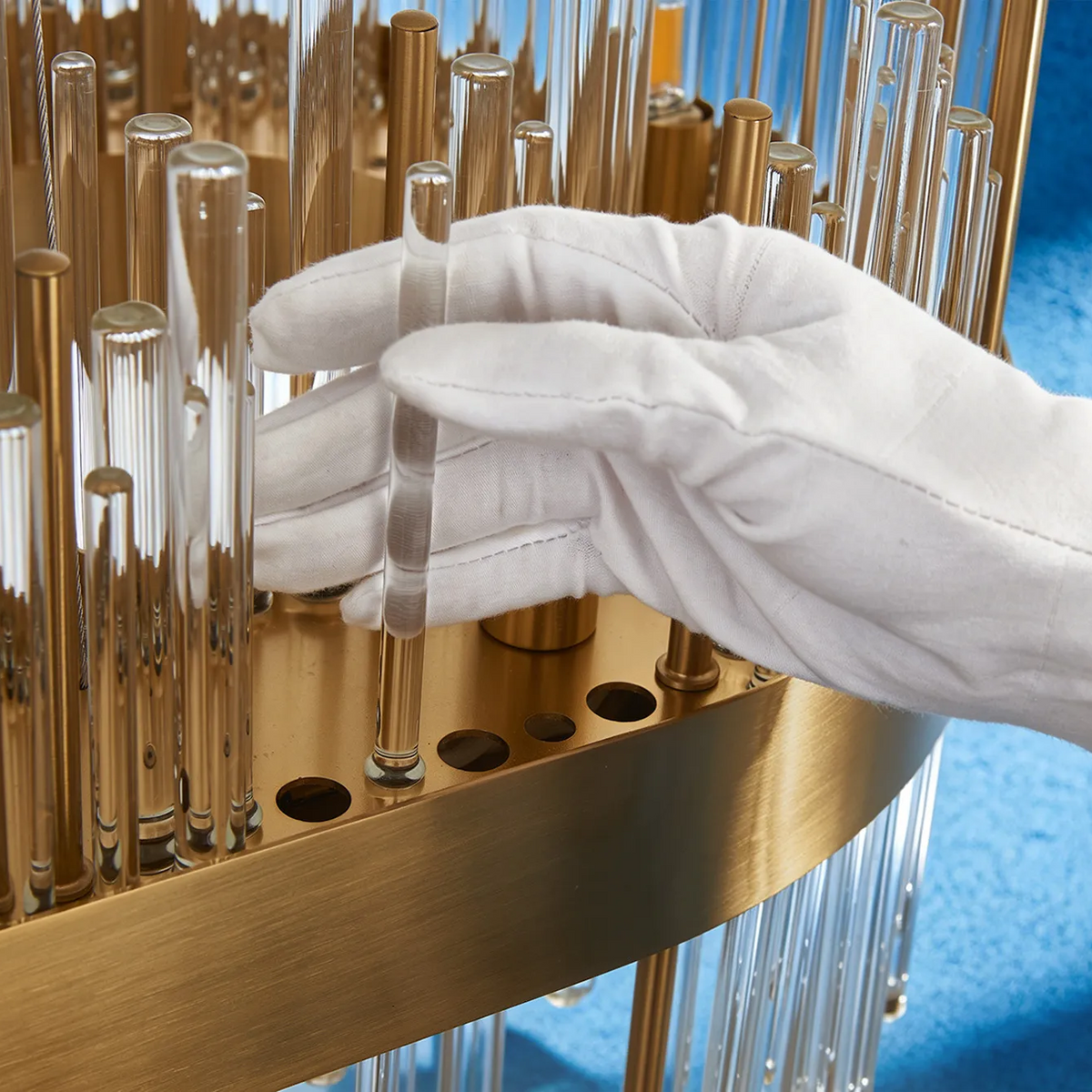Gloved hand placing a glass rod into a brass chandelier frame