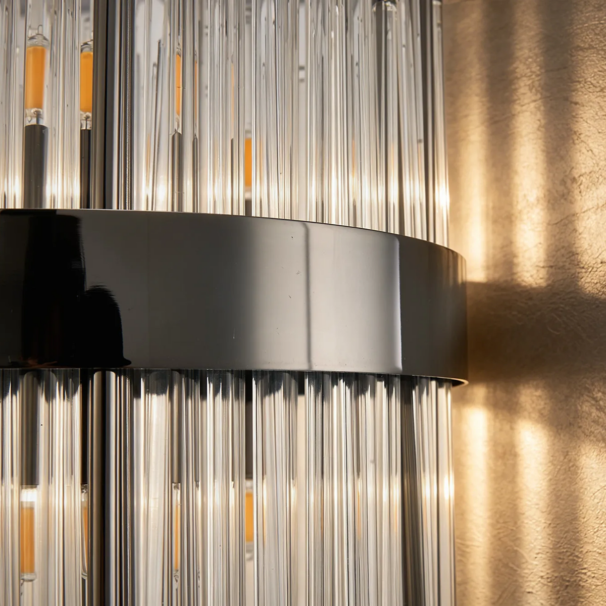 Close up of a wall light with clear glass rods and a dark metal band