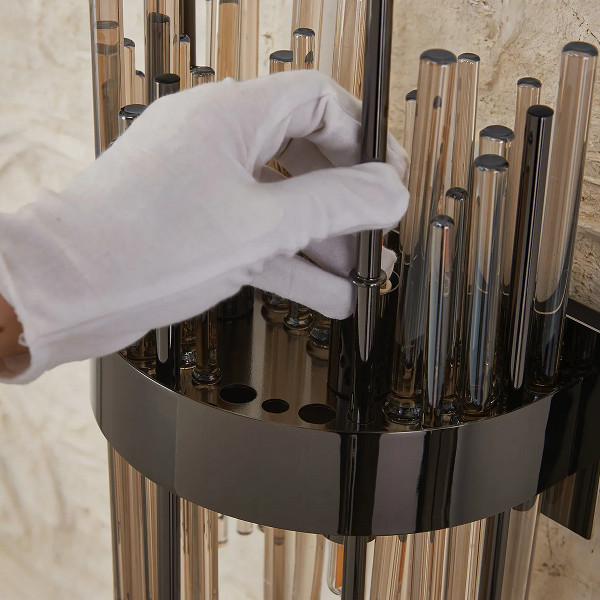 Gloved hand inserting a dark glass rod into a black metal base with other glass rods