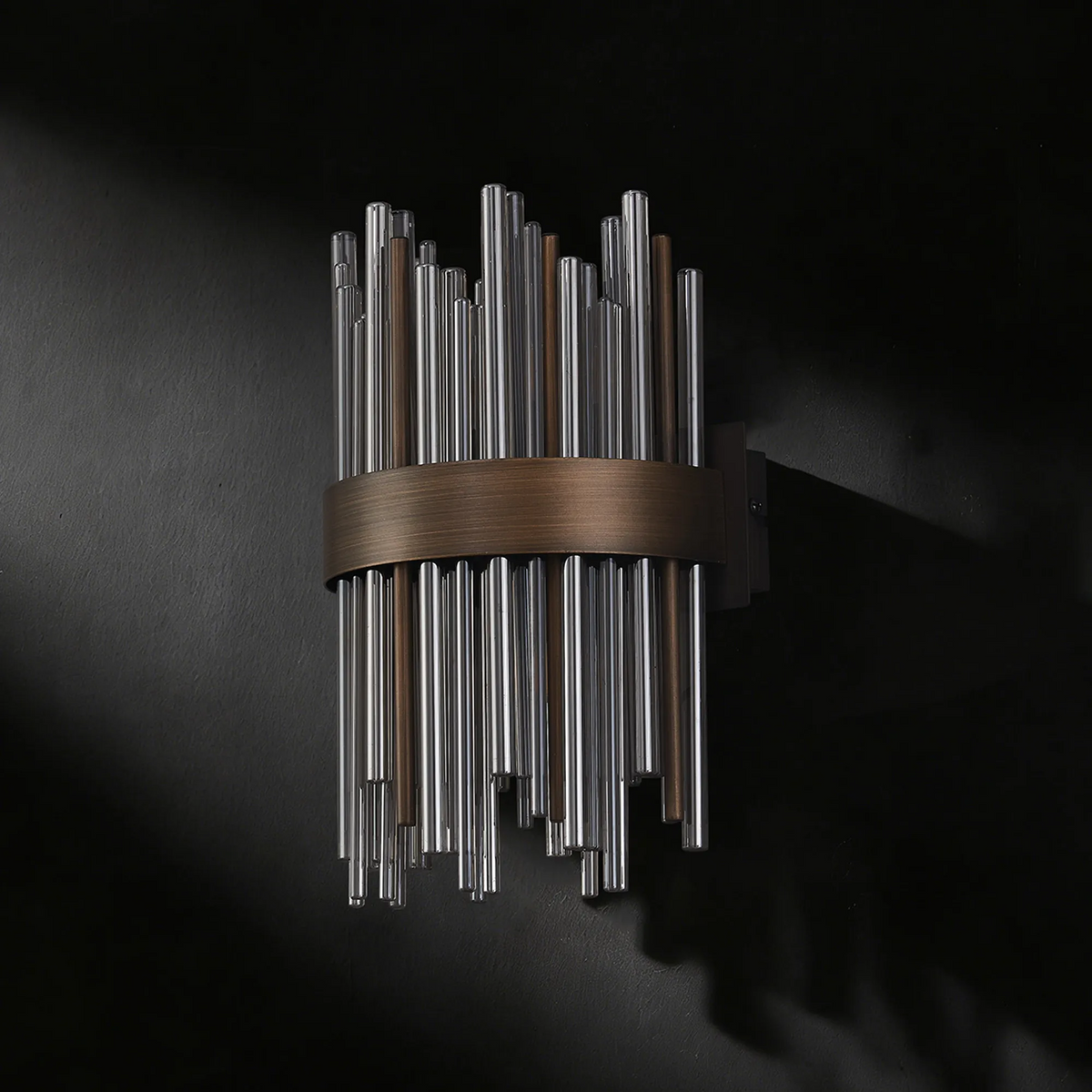 Wall sconce with clear and bronze glass rods arranged vertically around a bronze band