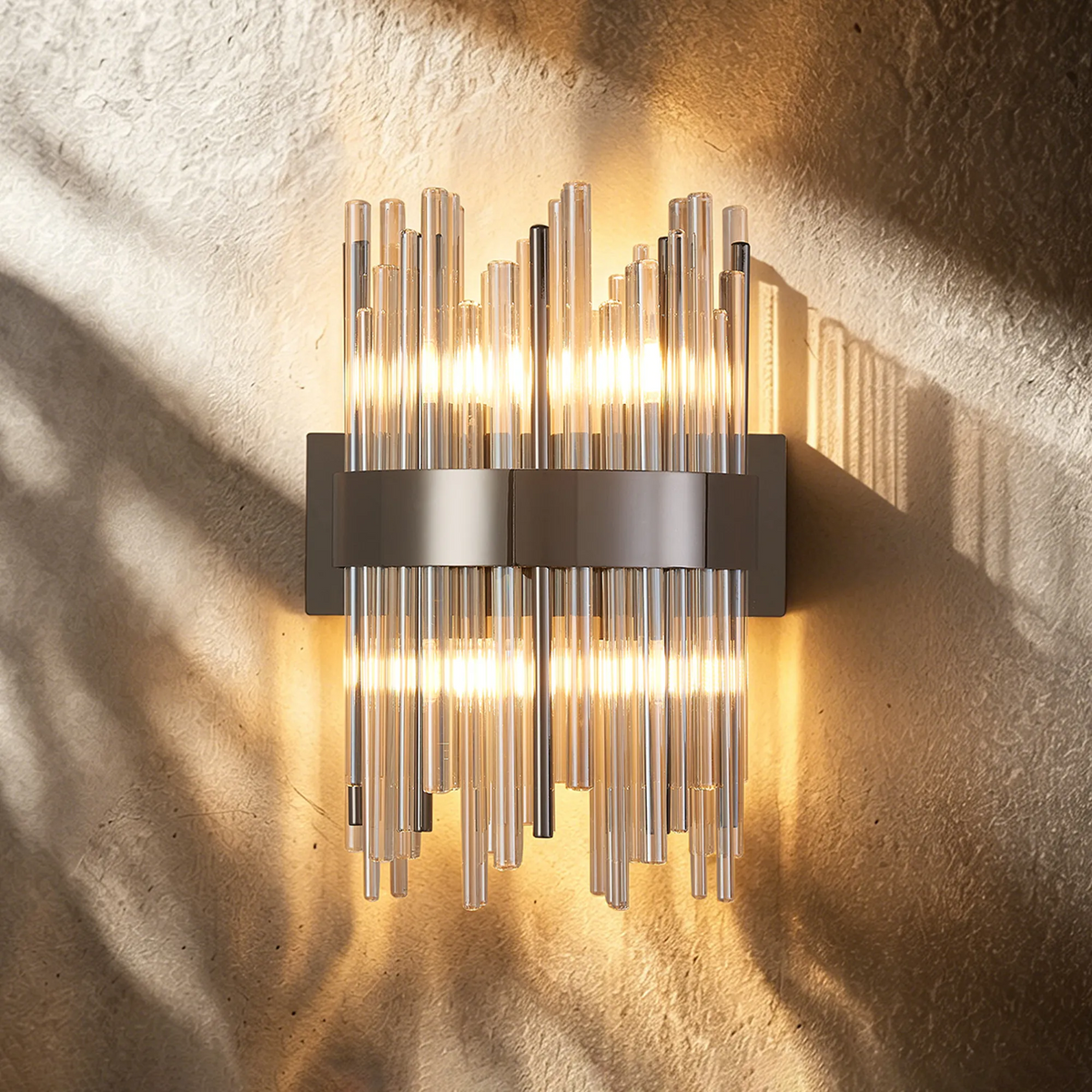 Modern wall sconce with vertical glass rods and a metallic band, illuminated against a textured wall