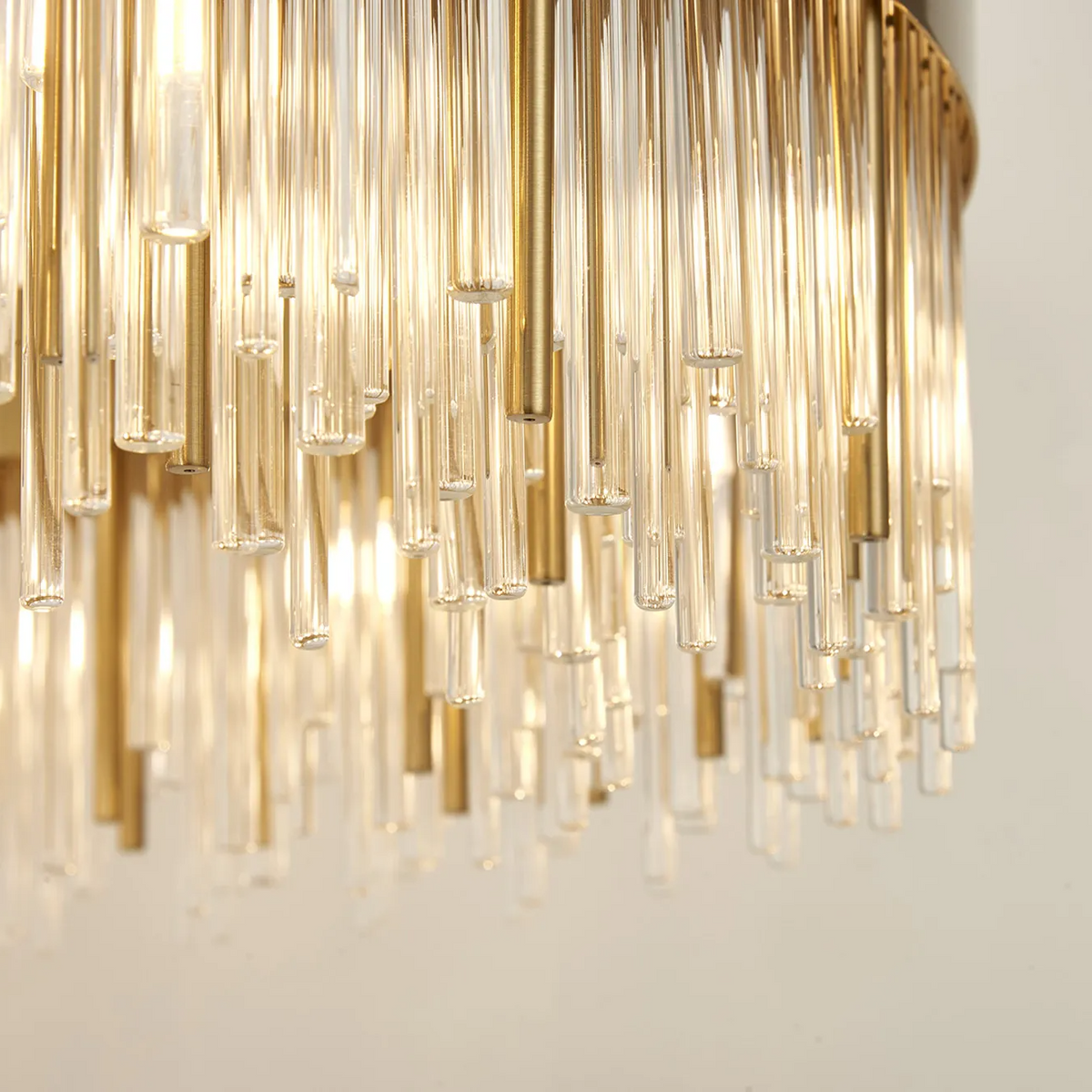 Close up of a chandelier with many glass tubes and brass rods hanging down, illuminated from above