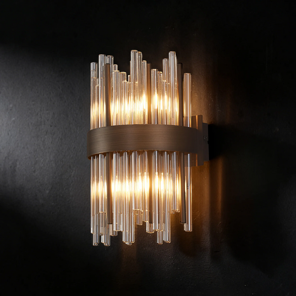 Wall sconce with vertical glass rods and a bronze band, illuminated against a dark wall