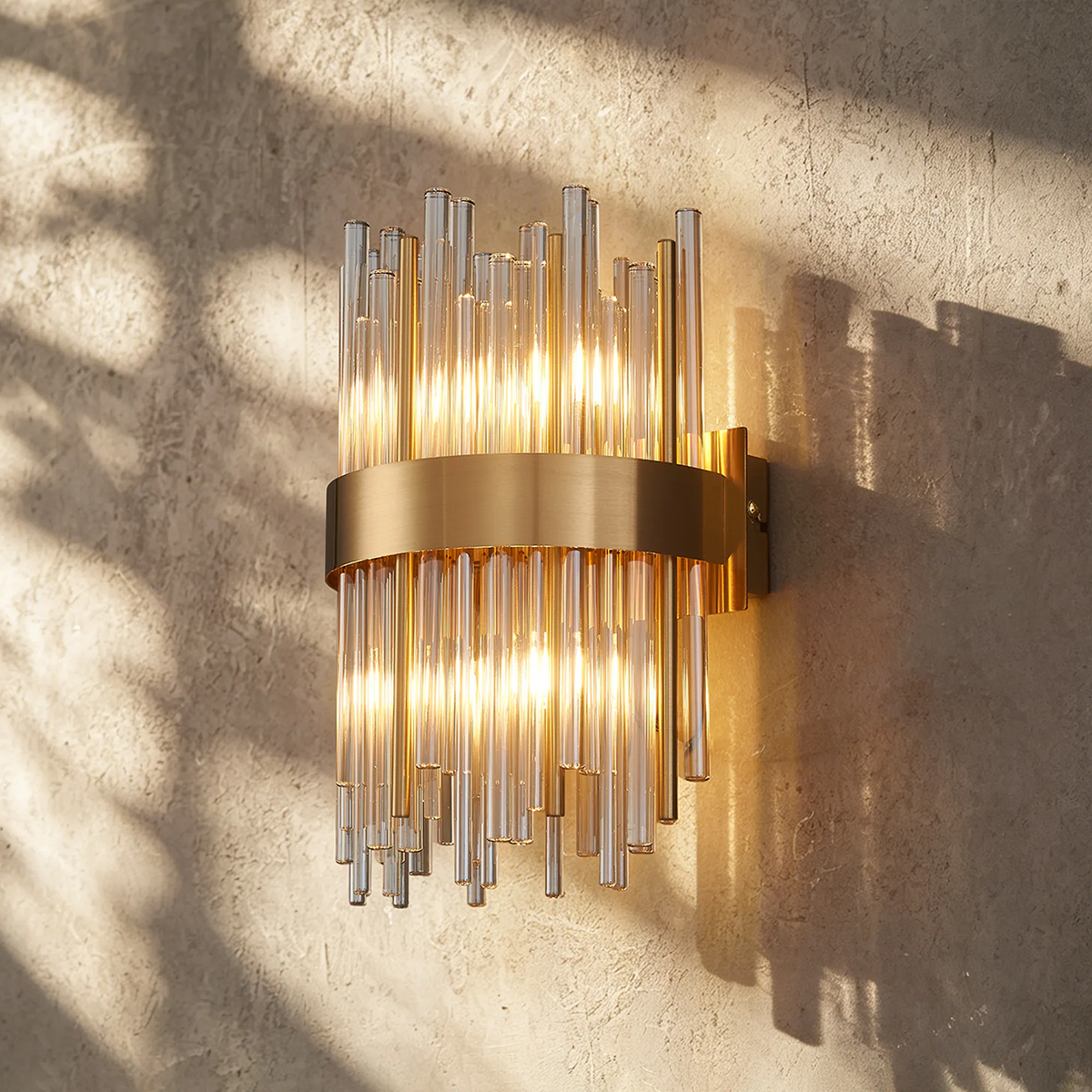 Gold wall sconce with clear glass rods on a textured wall