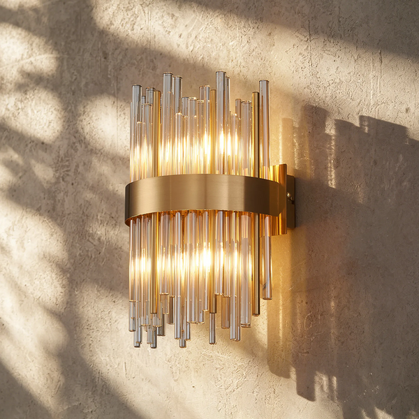 Gold wall sconce with clear glass rods on a textured wall