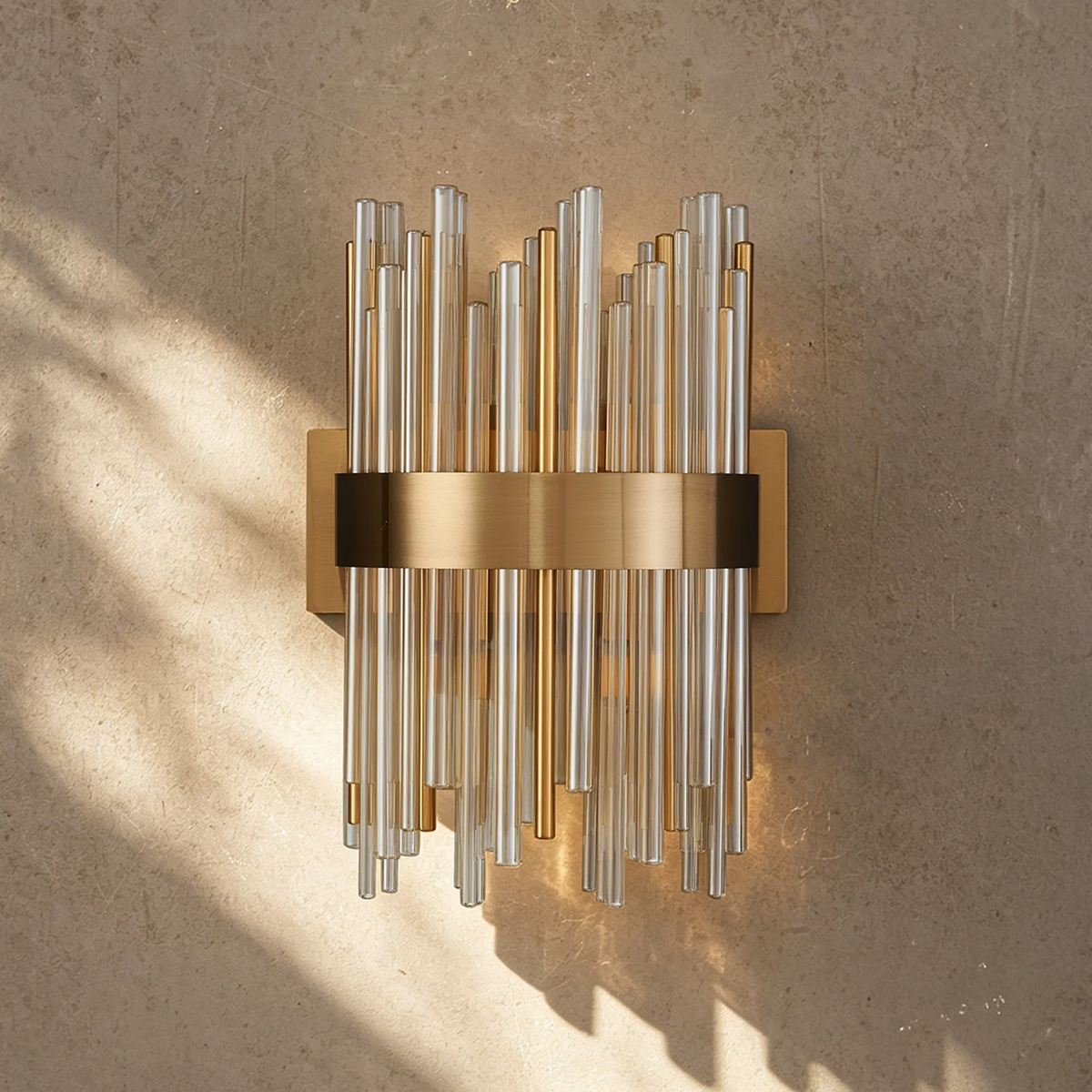 Gold and clear glass tube wall sconce on a textured beige wall